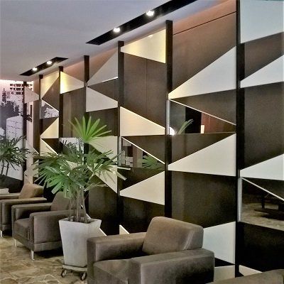 Una habitación con sillas y una planta frente a una pared con triángulos.