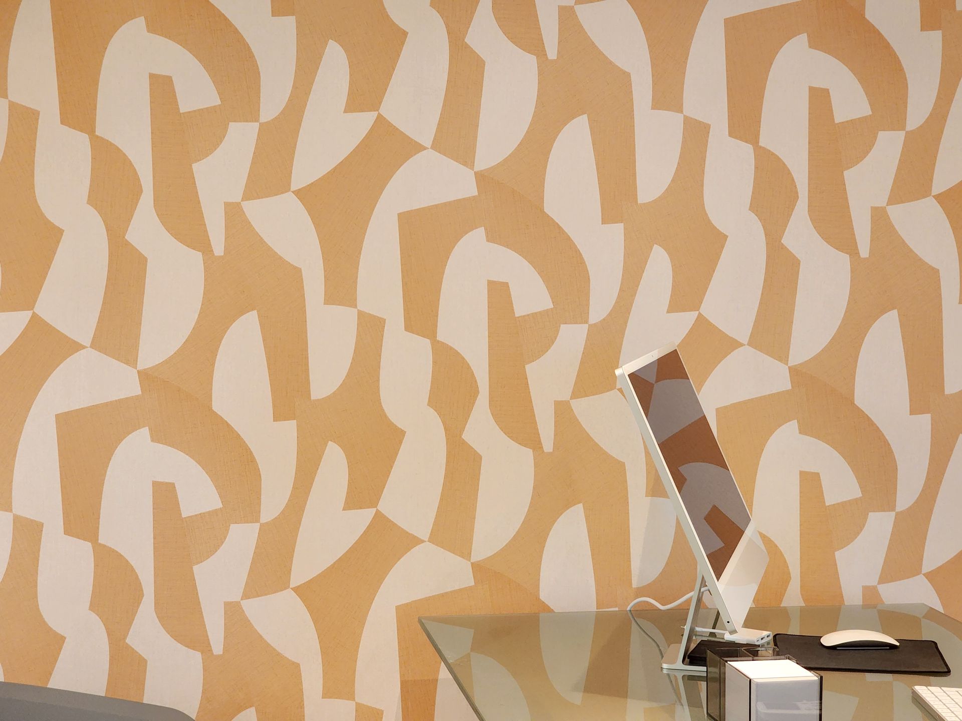 Una computadora está sobre un escritorio frente a una pared con un patrón en ella.