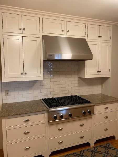 White kitchen cabinets with stainless steel range hood and cooktop.