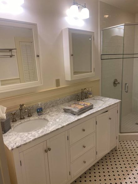 Bathroom with white vanity, marble countertop, dual sinks, and glass shower.