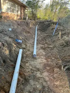 Two white pipes are sitting in the dirt next to a house.