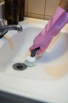 A person wearing pink gloves is cleaning a sink with a brush.