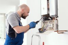 A man is fixing a boiler with a screwdriver.