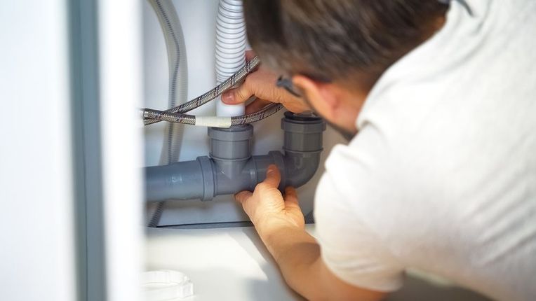 A man is fixing a sink pipe in a bathroom.