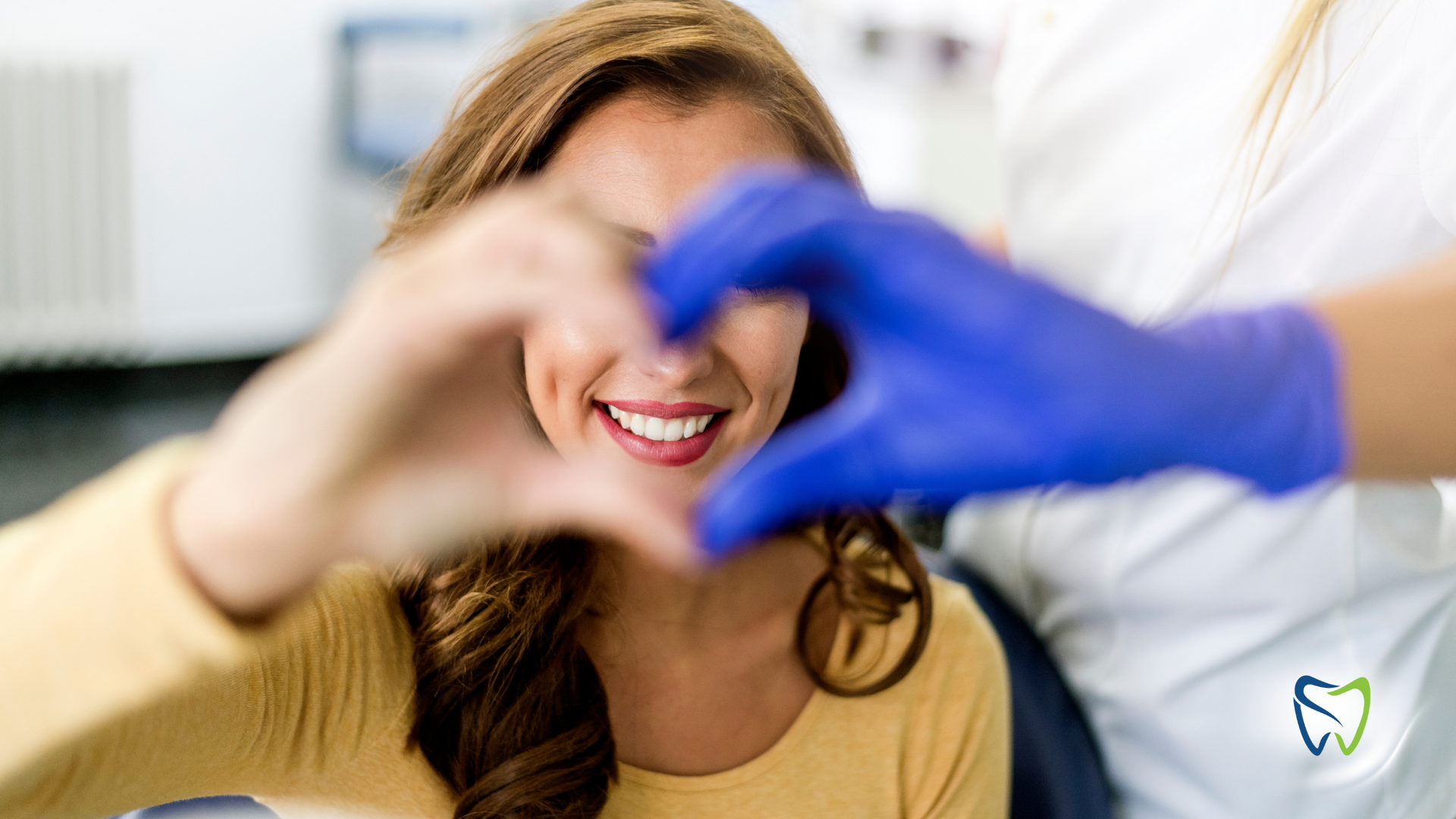 A woman is making a heart shape with her hands in a dental office.