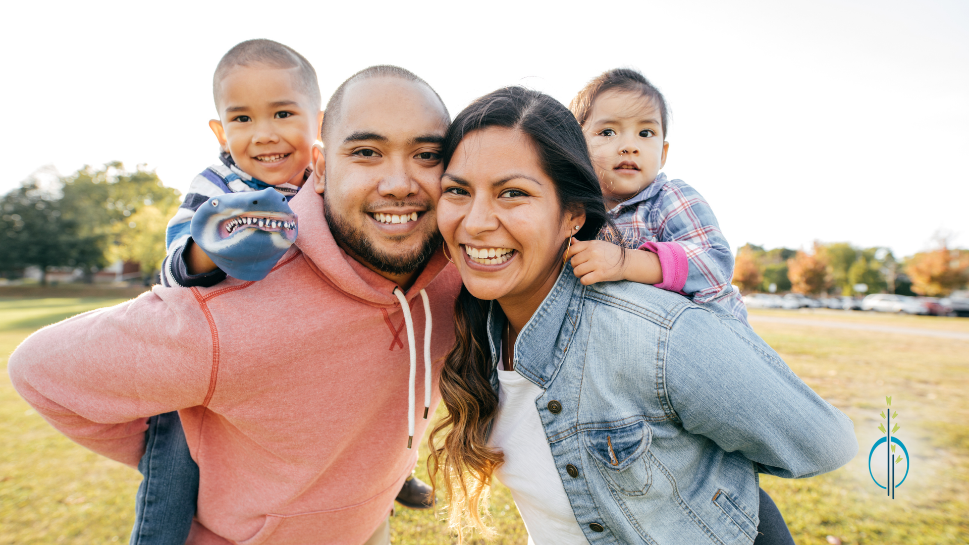 A man and woman are carrying two children on their shoulders in a park.