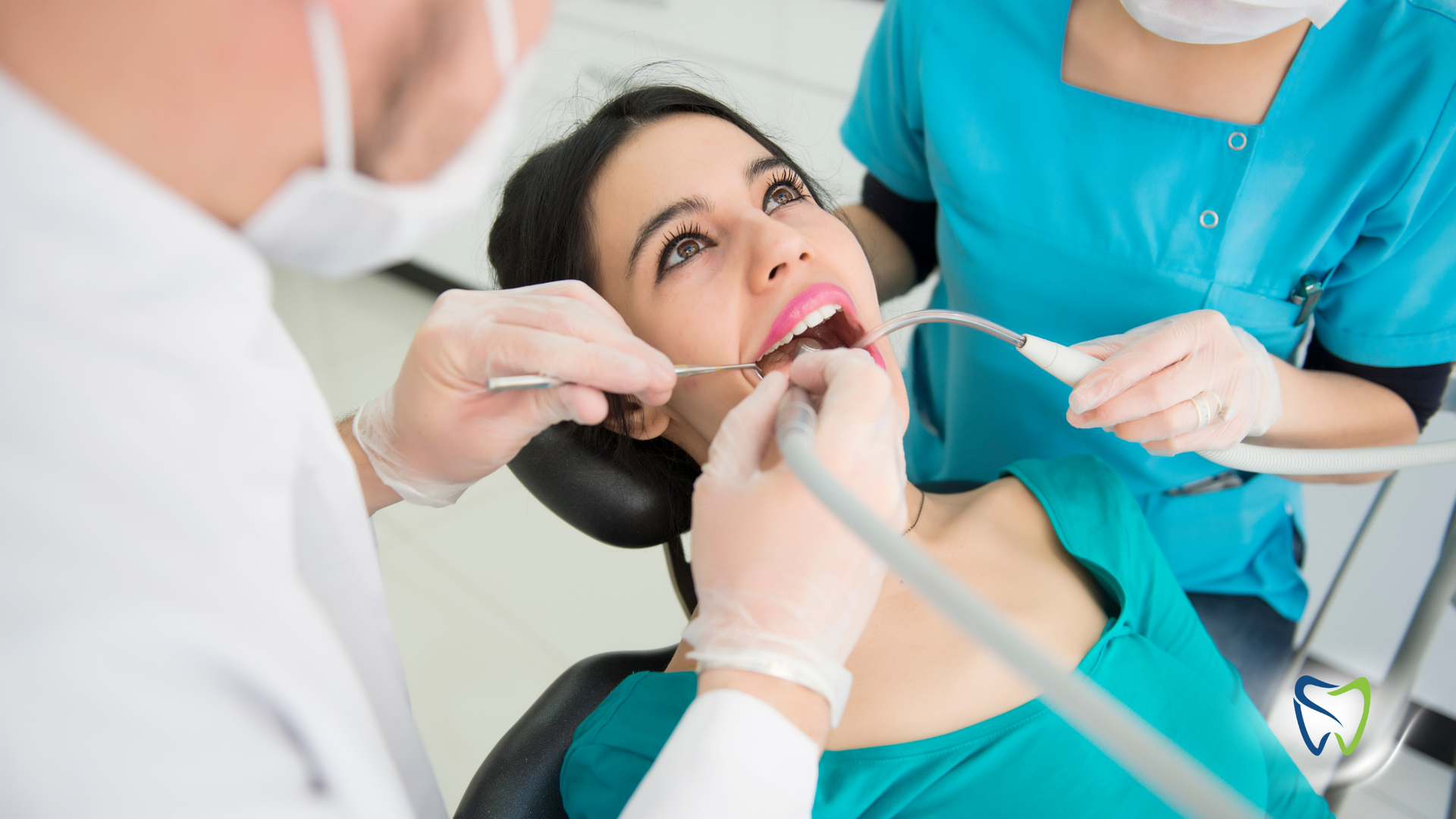 A woman is sitting in a dental chair while a dentist examines her teeth.