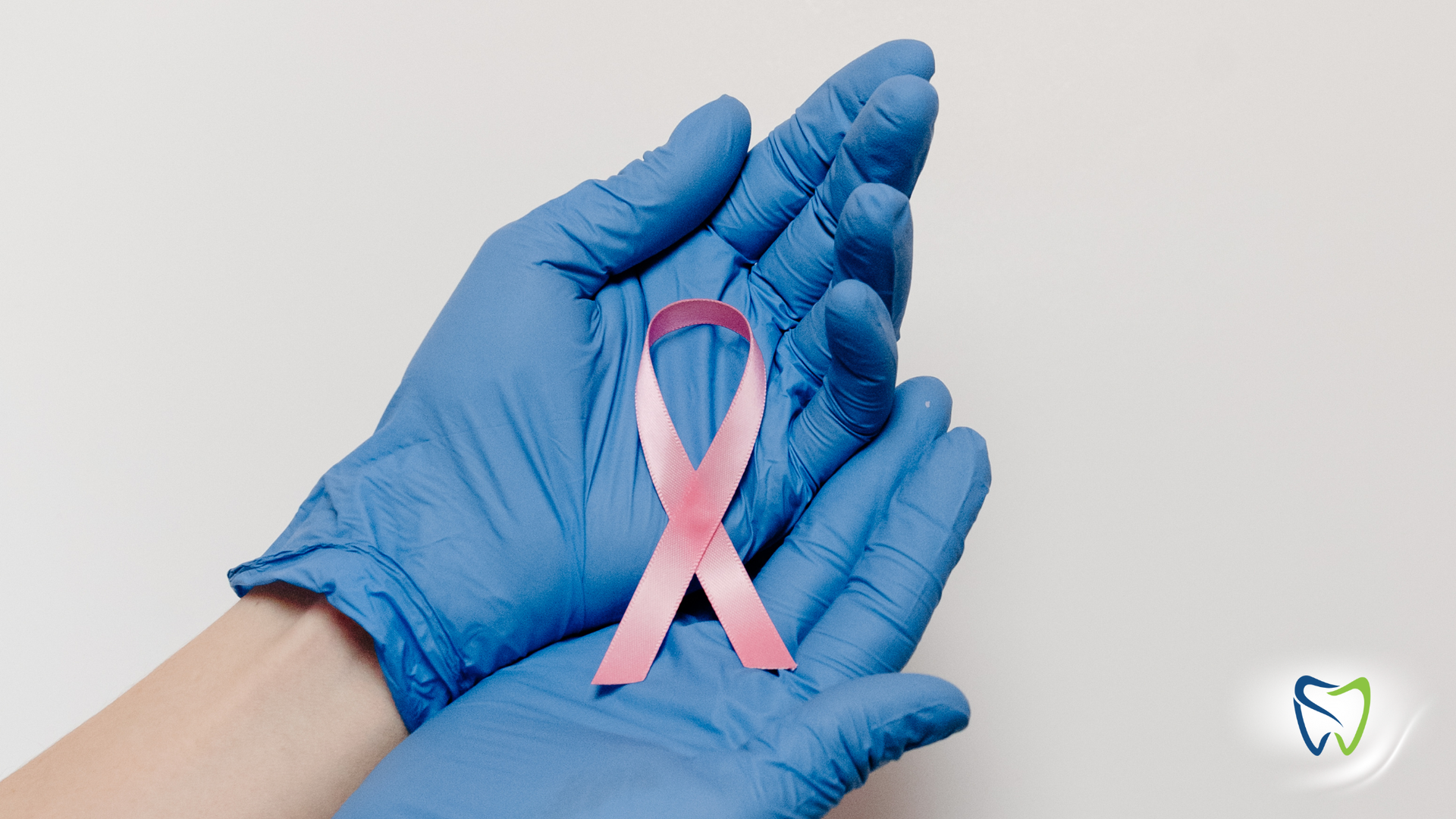 A person wearing blue gloves is holding a pink ribbon.