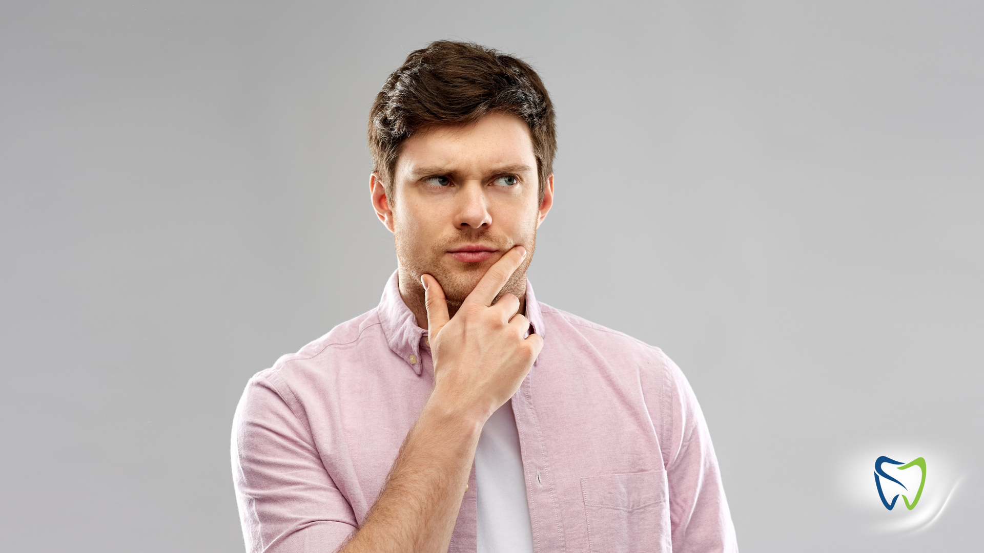 A man in a pink shirt is thinking with his hand on his chin.