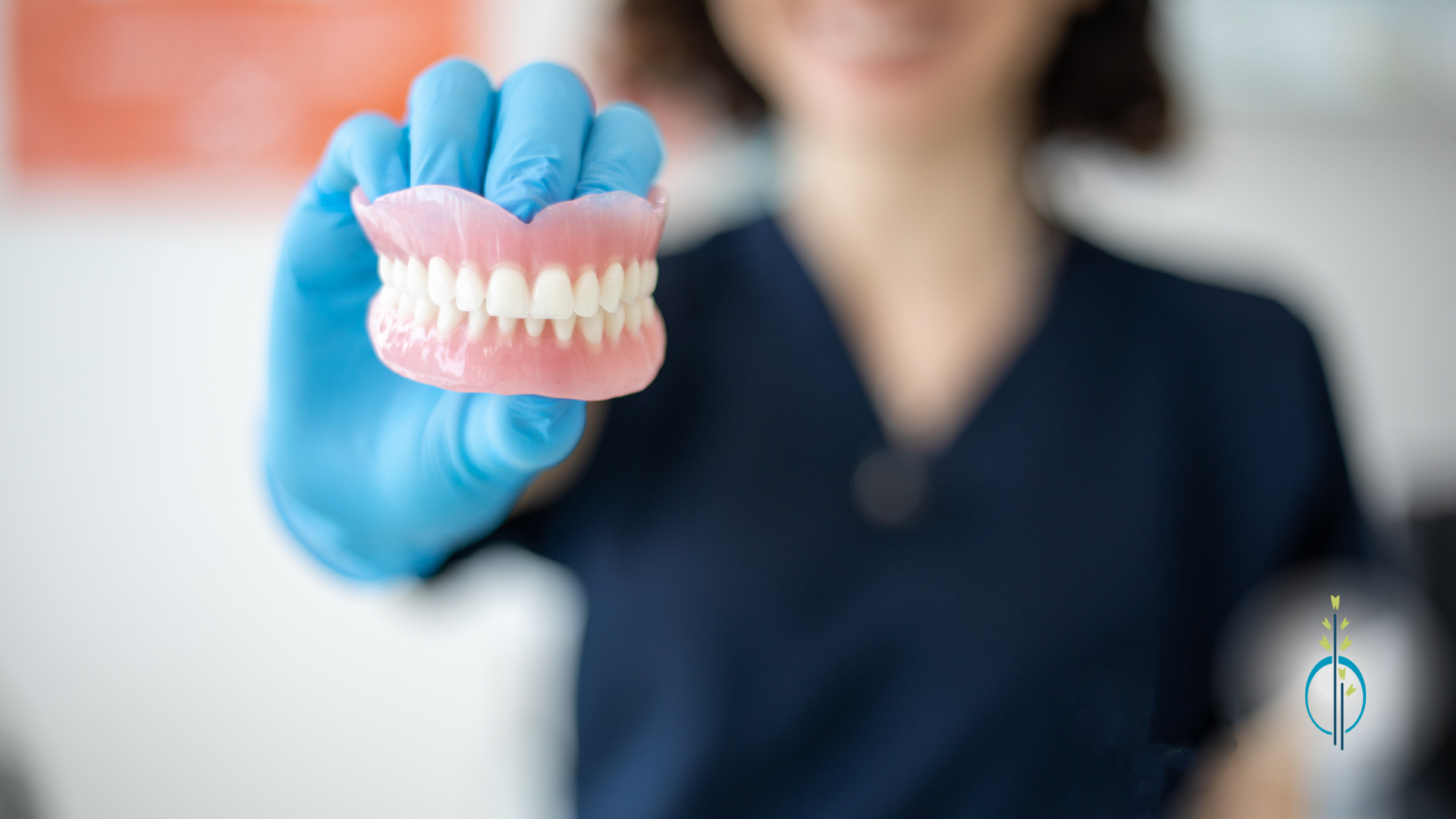 A woman wearing blue gloves is holding a denture in her hand.