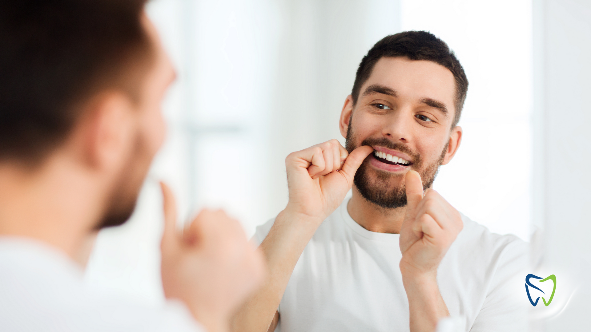 A man is flossing his teeth in front of a mirror.