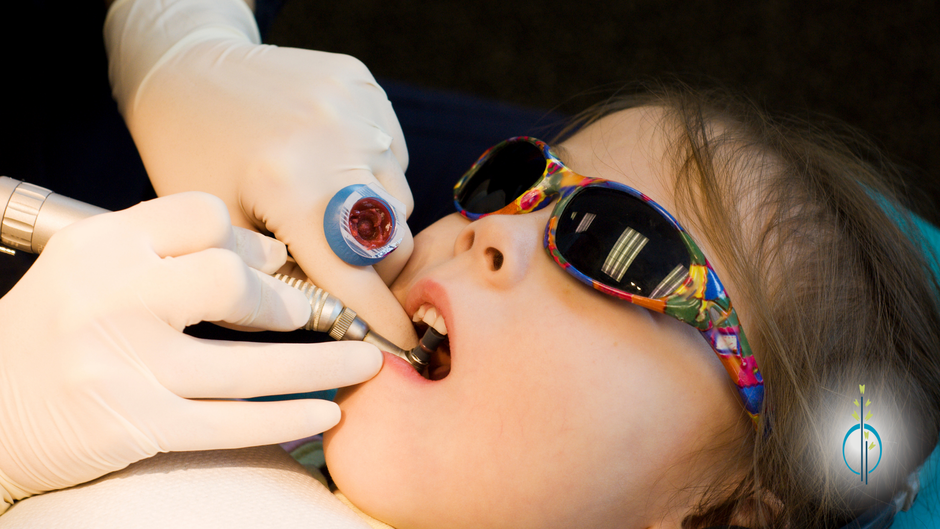 A young girl wearing sunglasses is getting her teeth examined by a dentist.