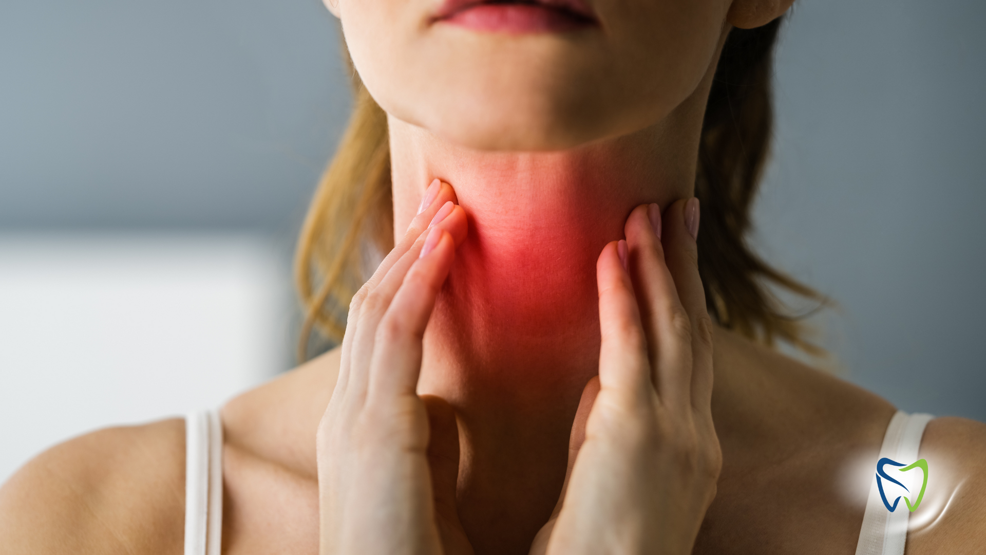 A woman is holding her neck in pain because she has a sore throat.