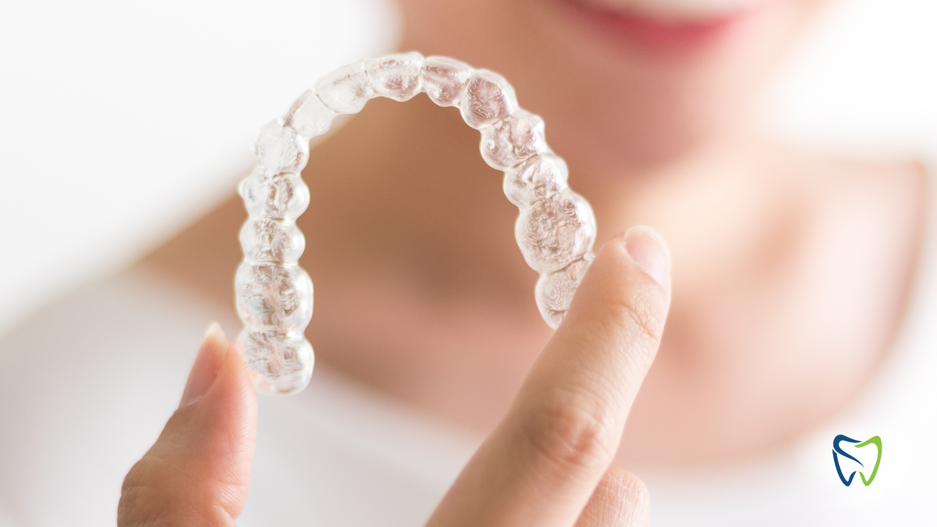 Person holding clear aligner, smiling, preparing to put it in mouth.