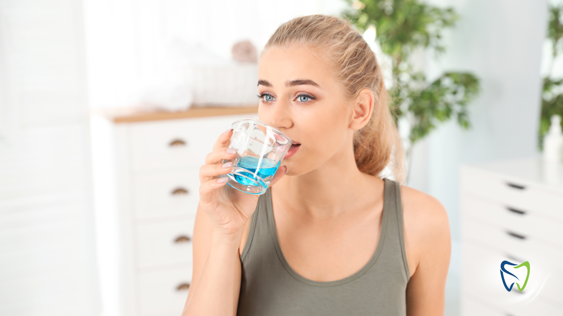 Woman drinking blue mouthwash in a bathroom setting.