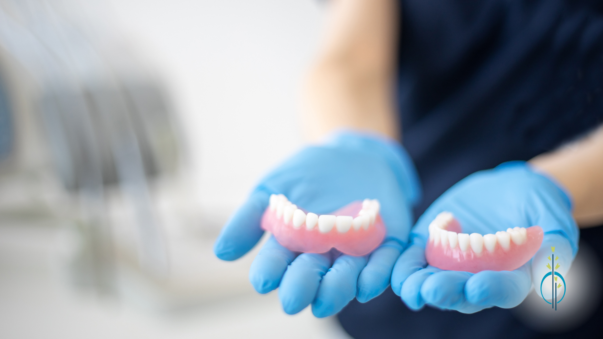 A person wearing blue gloves is holding two dentures in their hands.