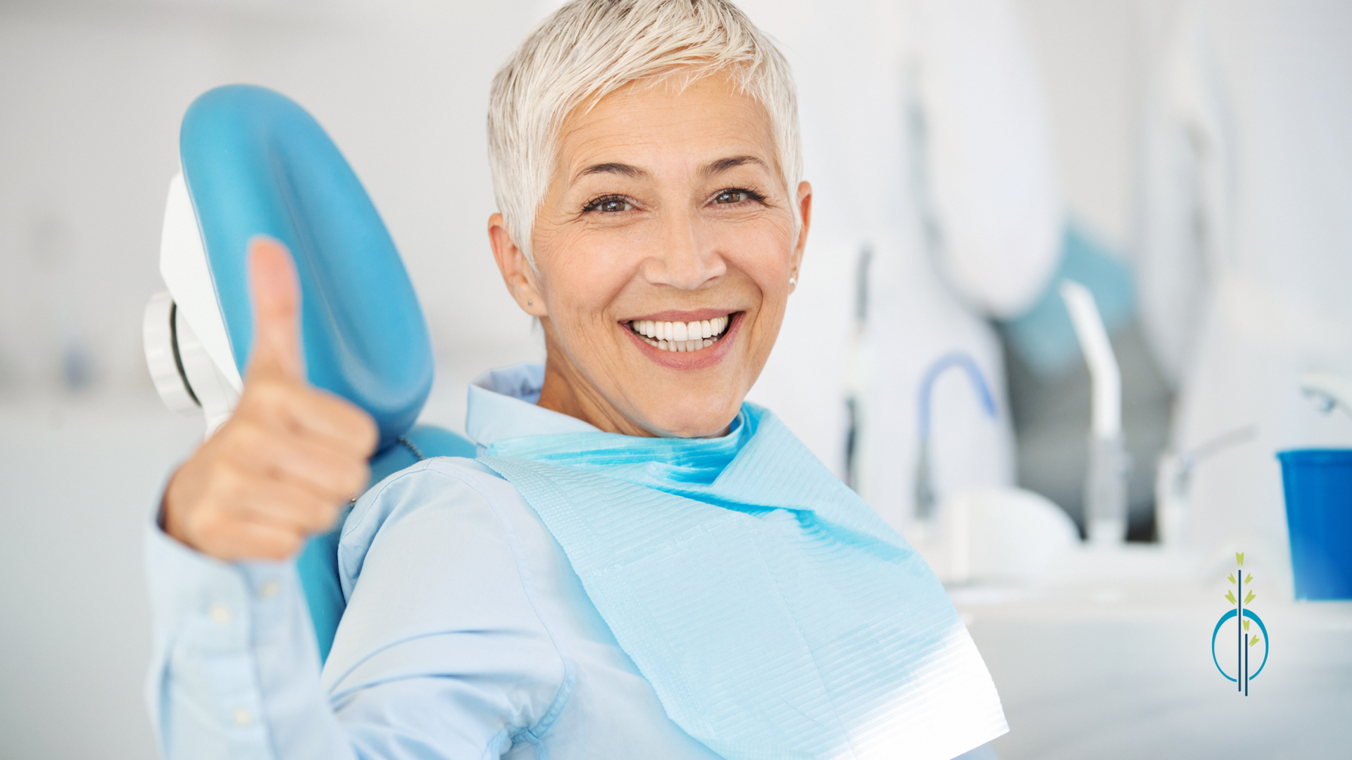 An older woman is sitting in a dental chair and giving a thumbs up.