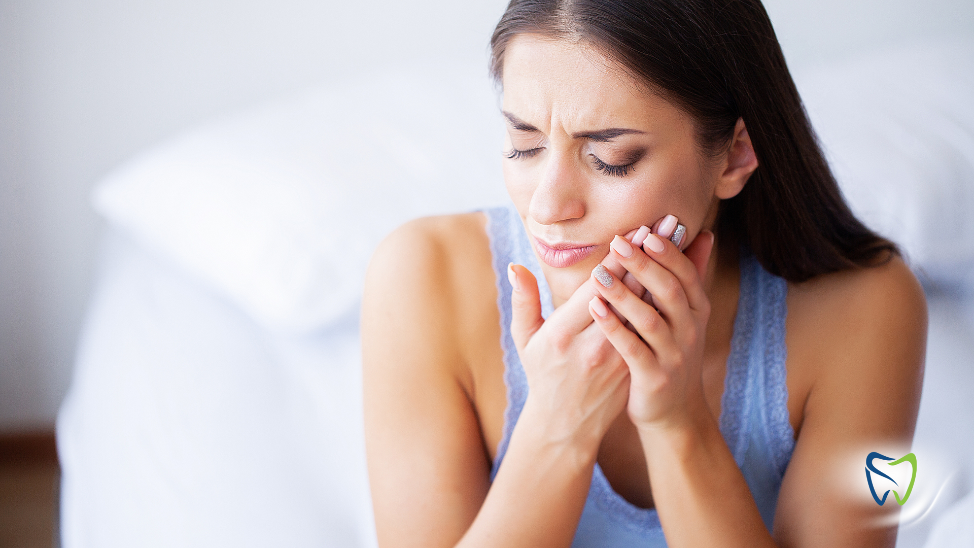 A woman is sitting on a bed with a toothache.