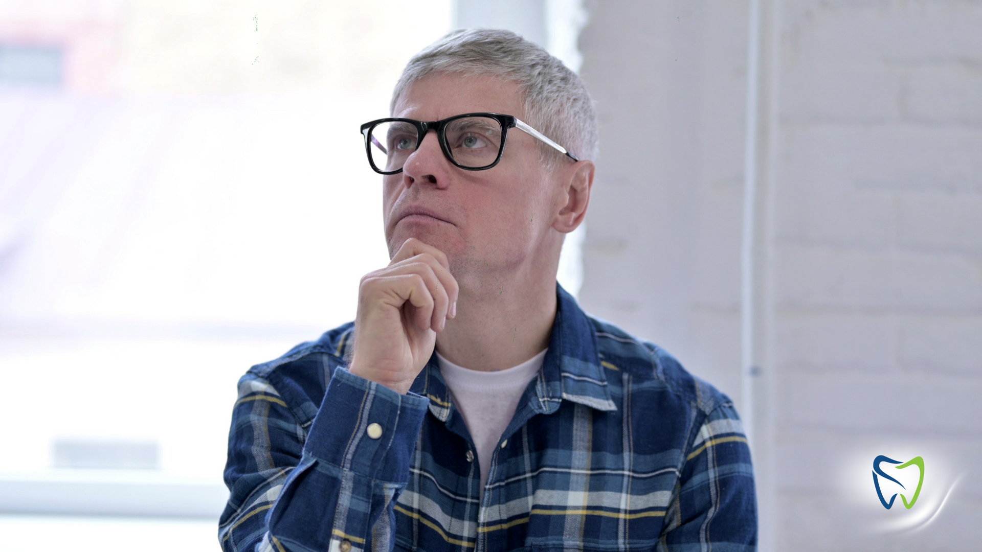An older man wearing glasses is sitting in front of a window.