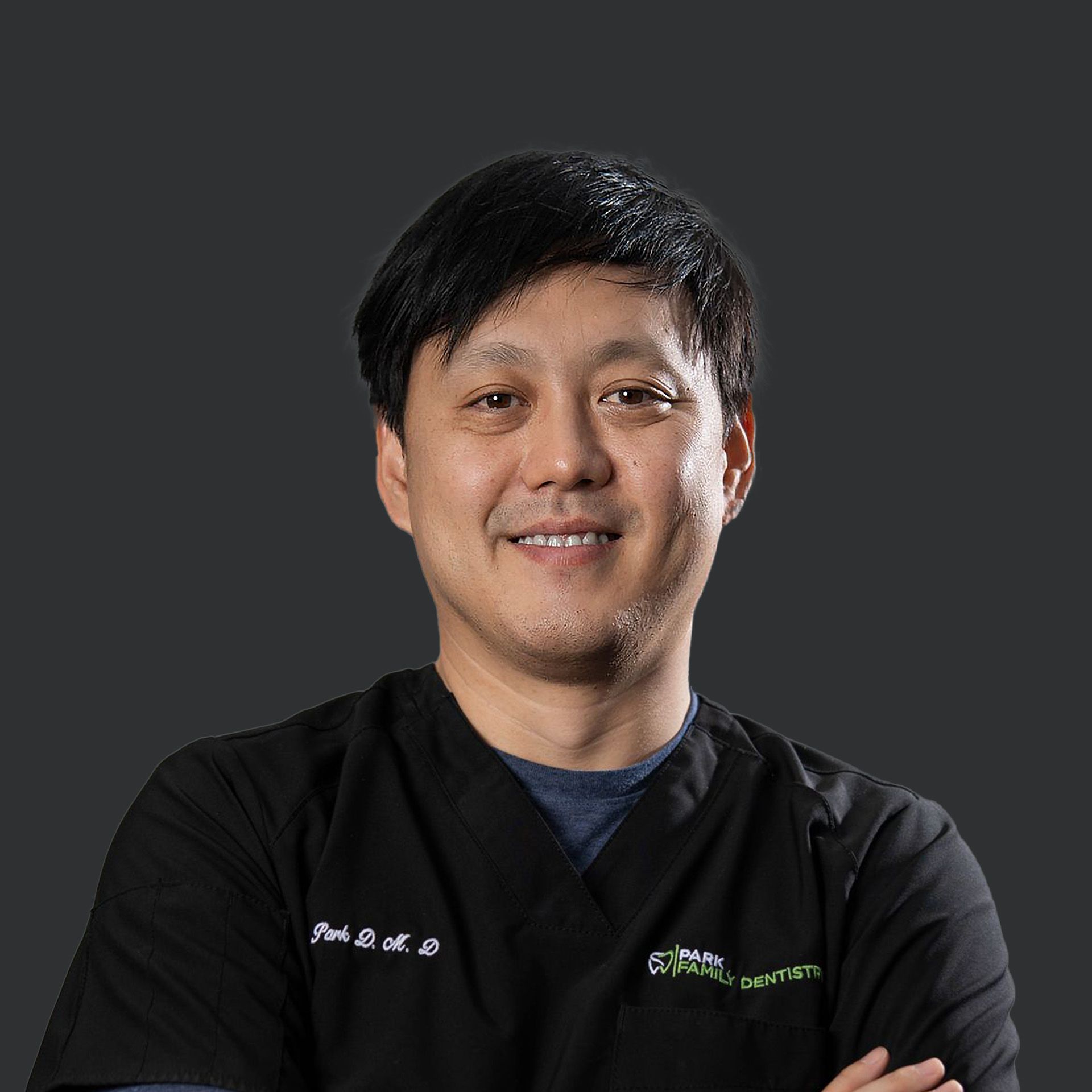 A man in a black scrub top is smiling with his arms crossed.
