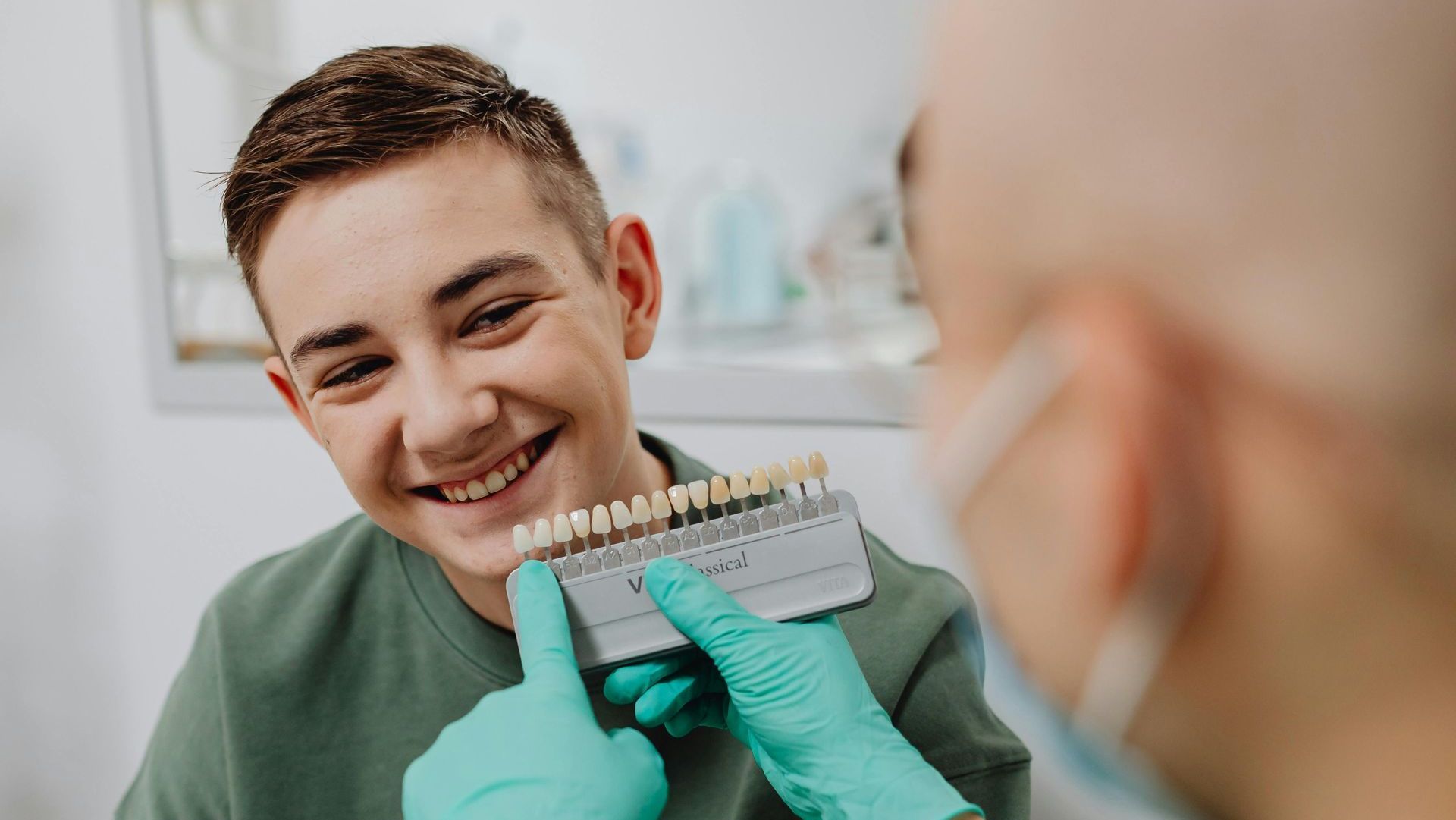 A young man is smiling while a dentist examines his teeth.