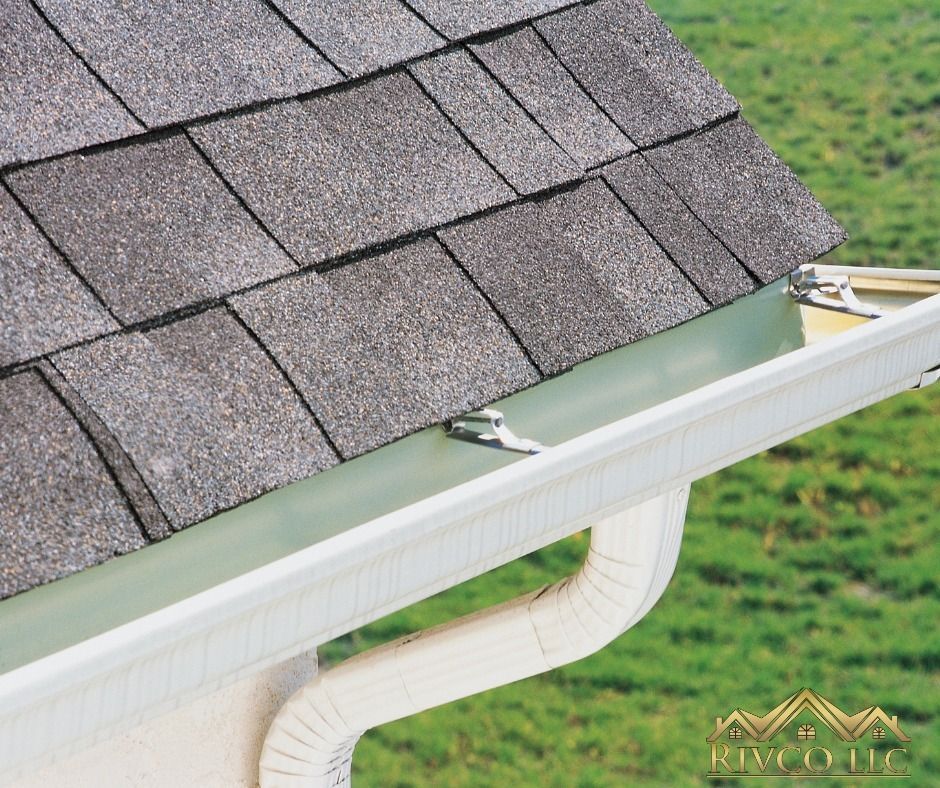 A white gutter is attached to a roof with shingles