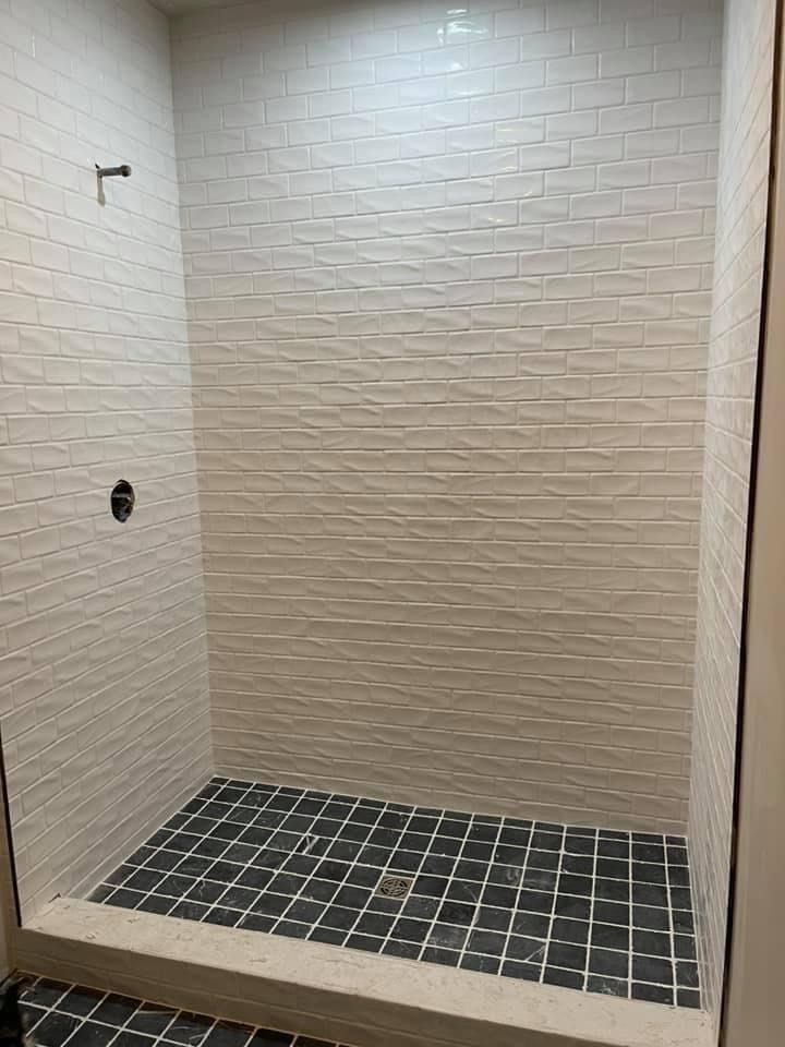 A shower stall with white tiles on the wall and black tiles on the floor.