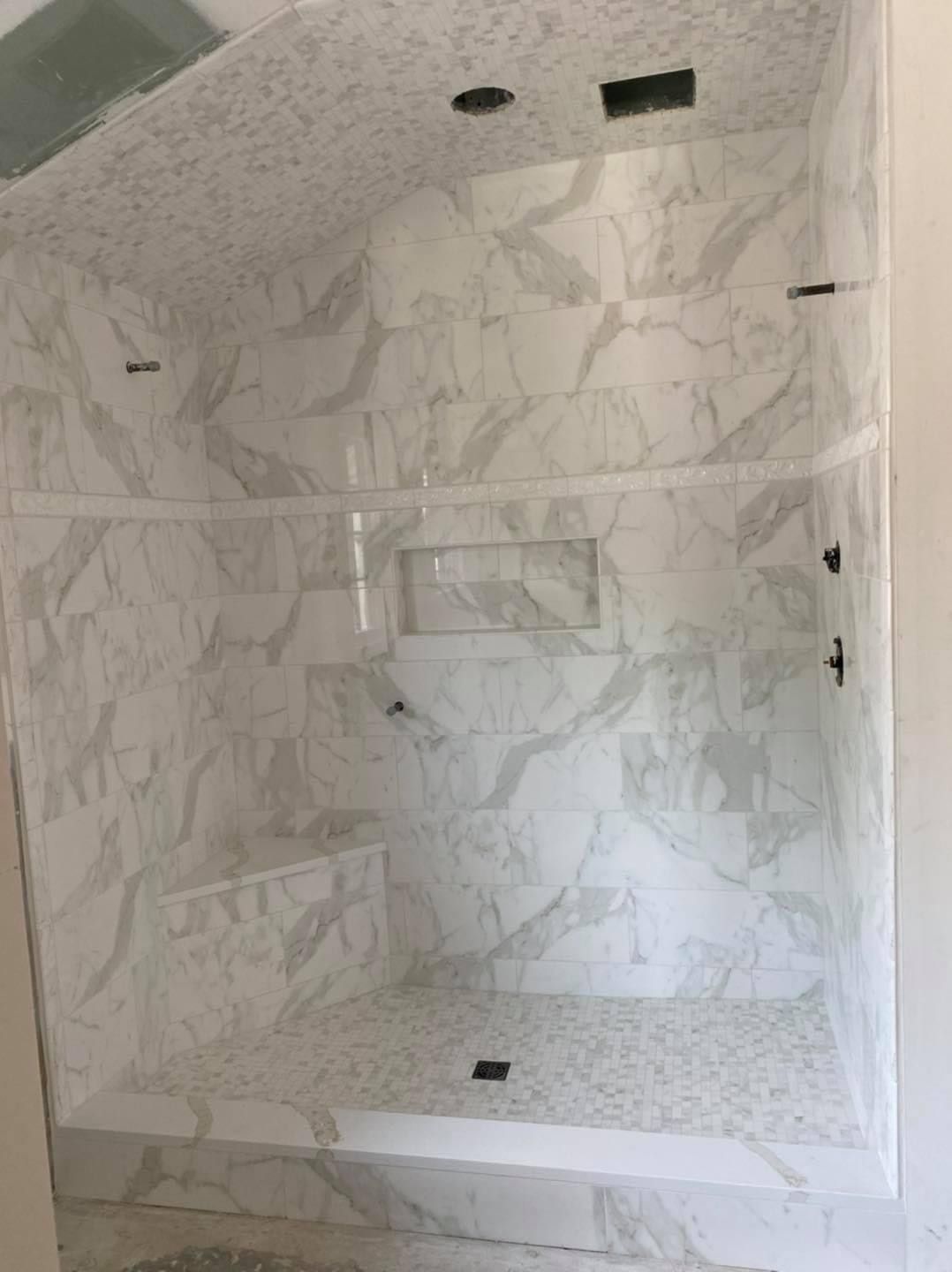 A bathroom with marble tiles and a walk in shower with a glass door.