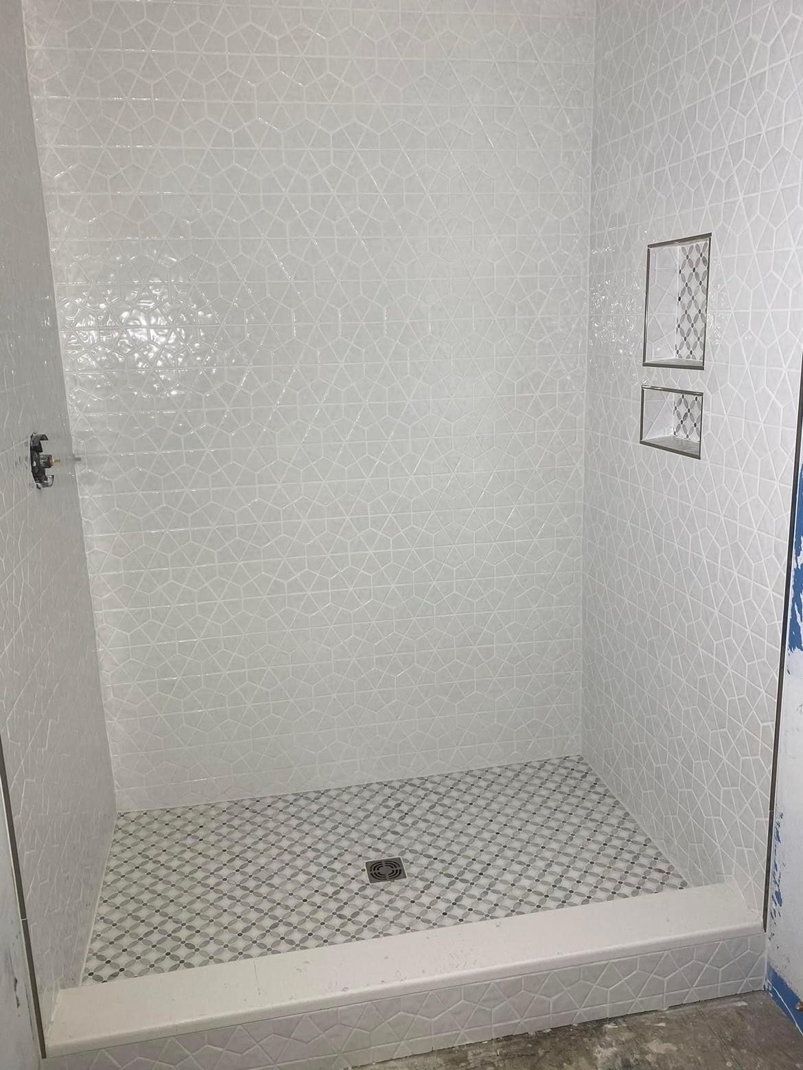 A shower stall with white tiles and a drain in a bathroom.