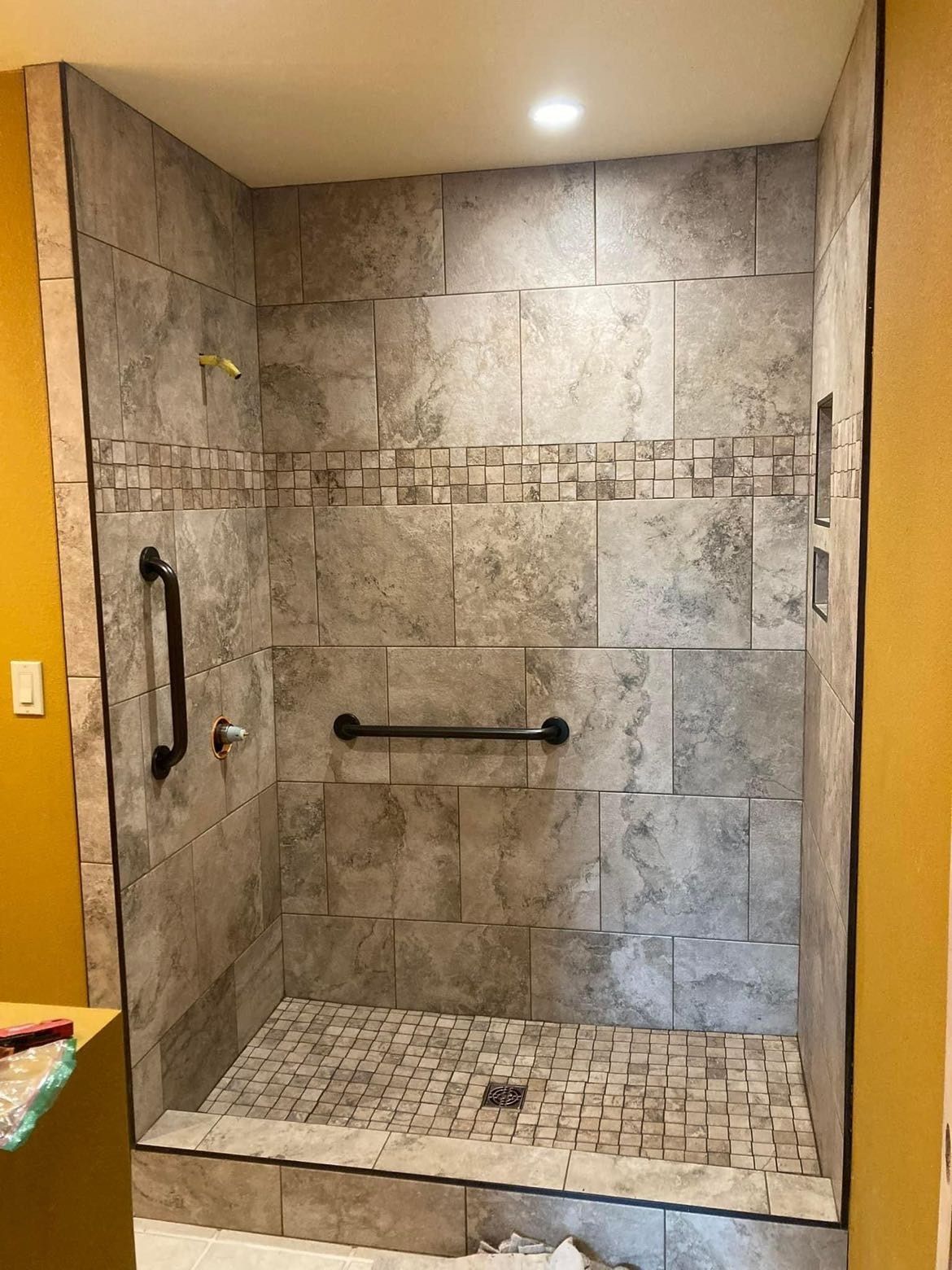 A bathroom with a walk in shower with a hand rail.
