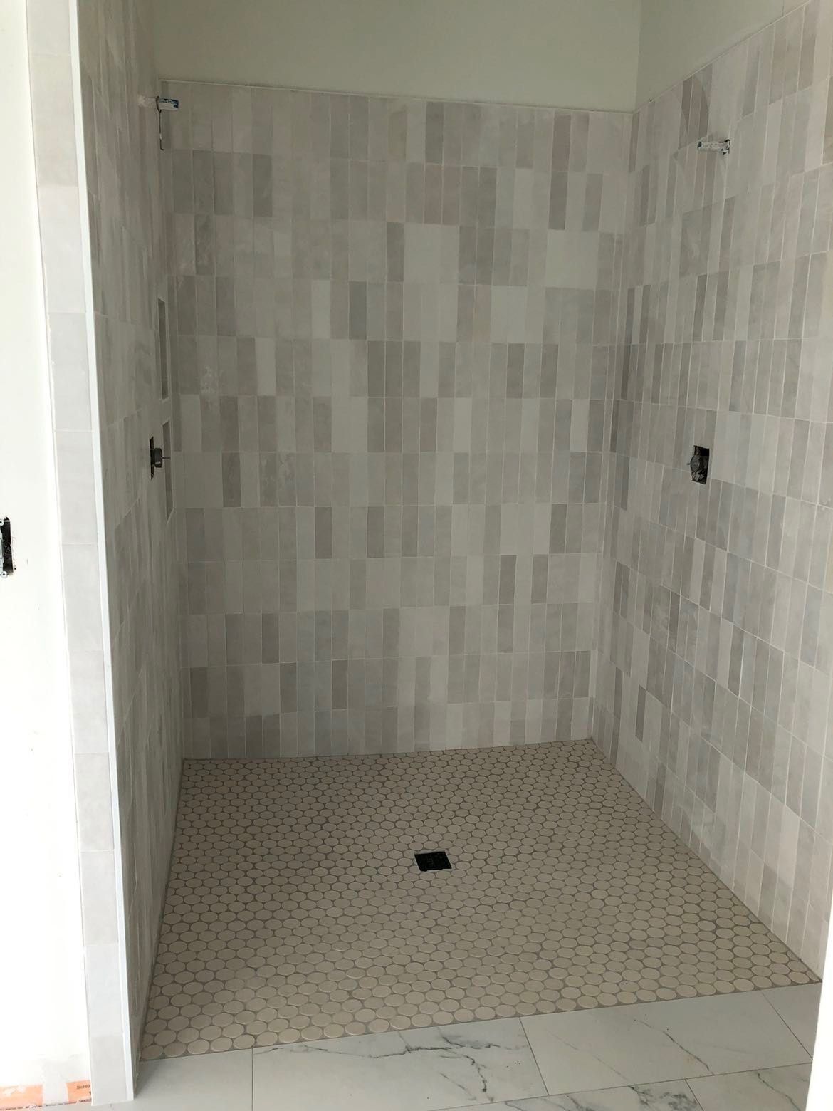 A shower stall with white tiles on the wall and floor.