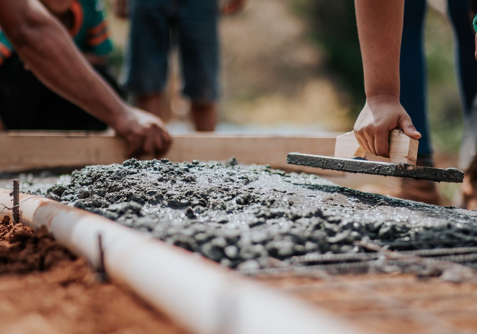 A person is using a trowel to spread concrete on the ground.