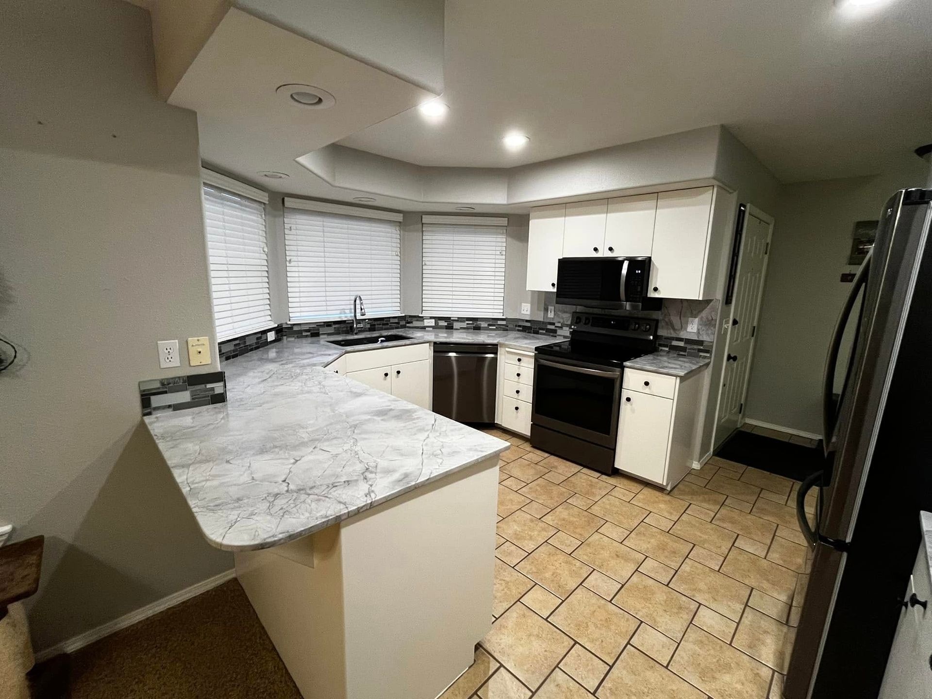 Kitchen with white cabinets, gray countertops, stainless steel appliances, and beige tile floor.