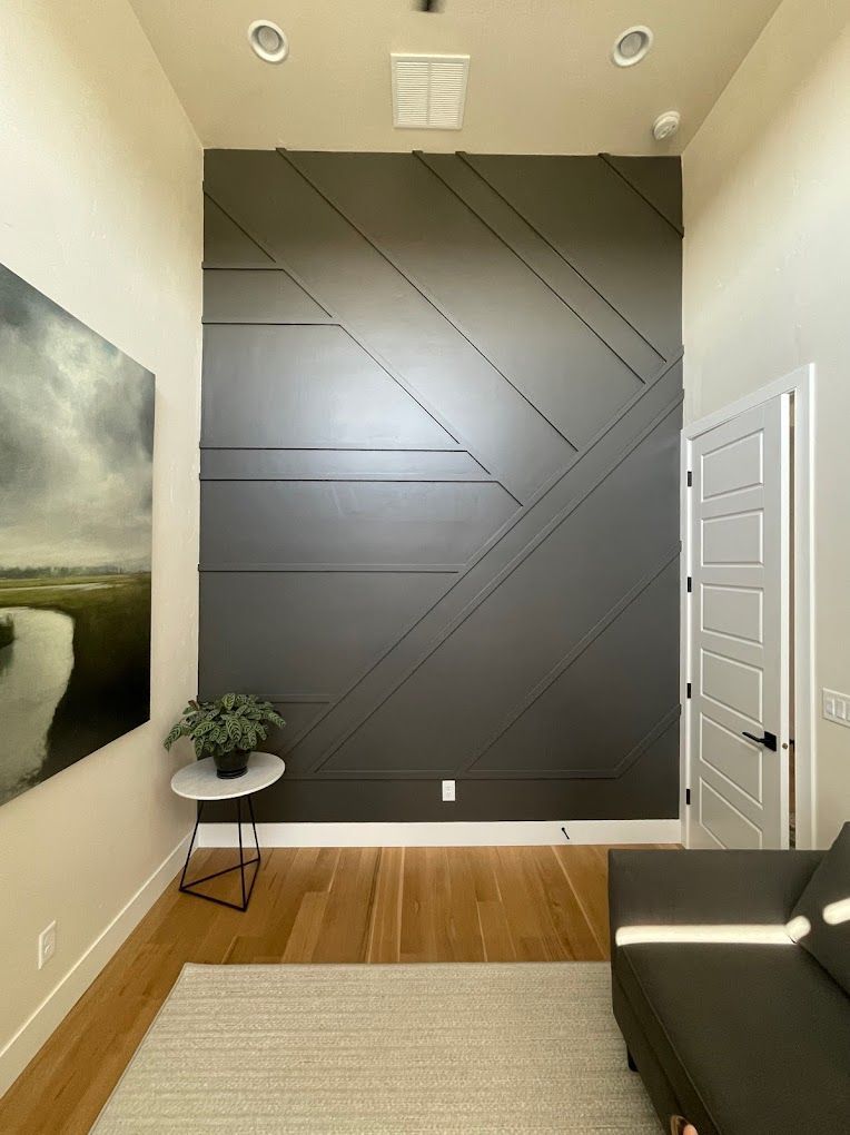 Gray accent wall with geometric design, painting, small table, and couch in a modern interior.