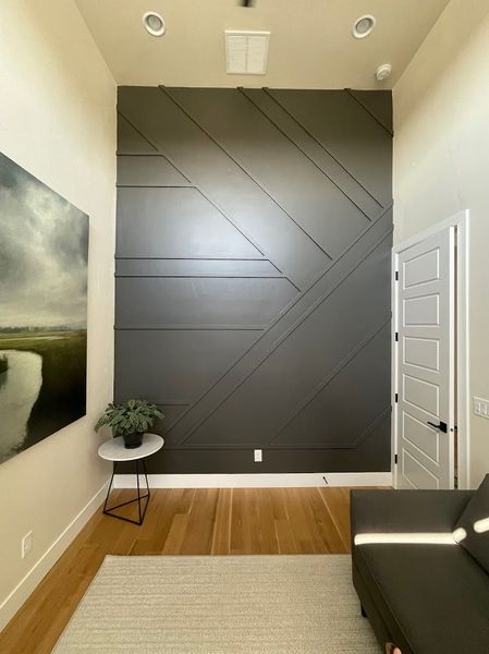 Gray accent wall with geometric design, painting, small table, and couch in a modern interior.