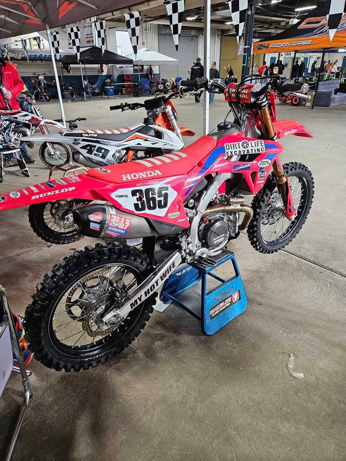 A red dirt bike with the number 365 on it is parked in a garage.