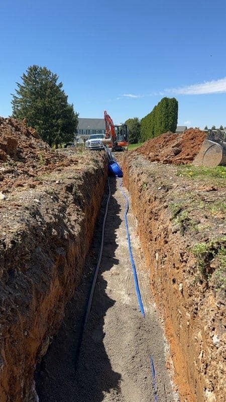 A blue pipe is being installed in a trench.