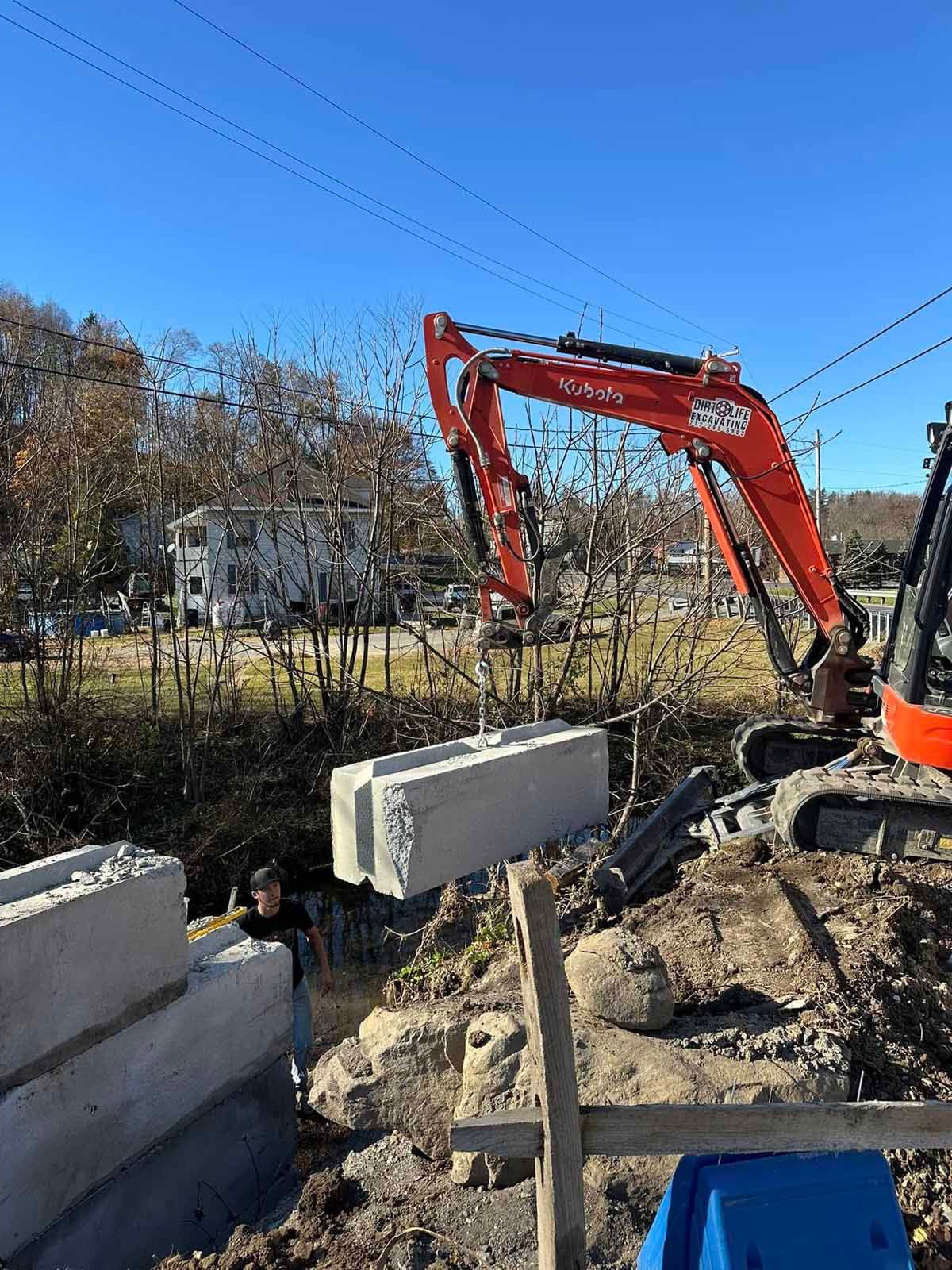 A red excavator is moving concrete blocks on a construction site.