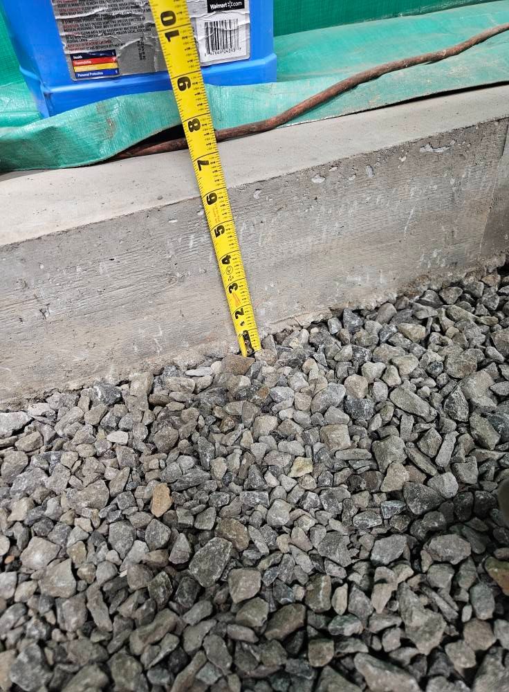 A yellow tape measure is sitting on top of a pile of gravel.
