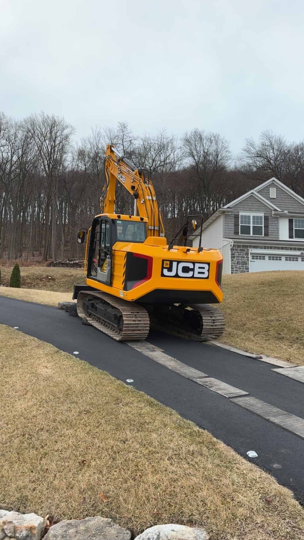 A yellow excavator is driving down a driveway next to a house.