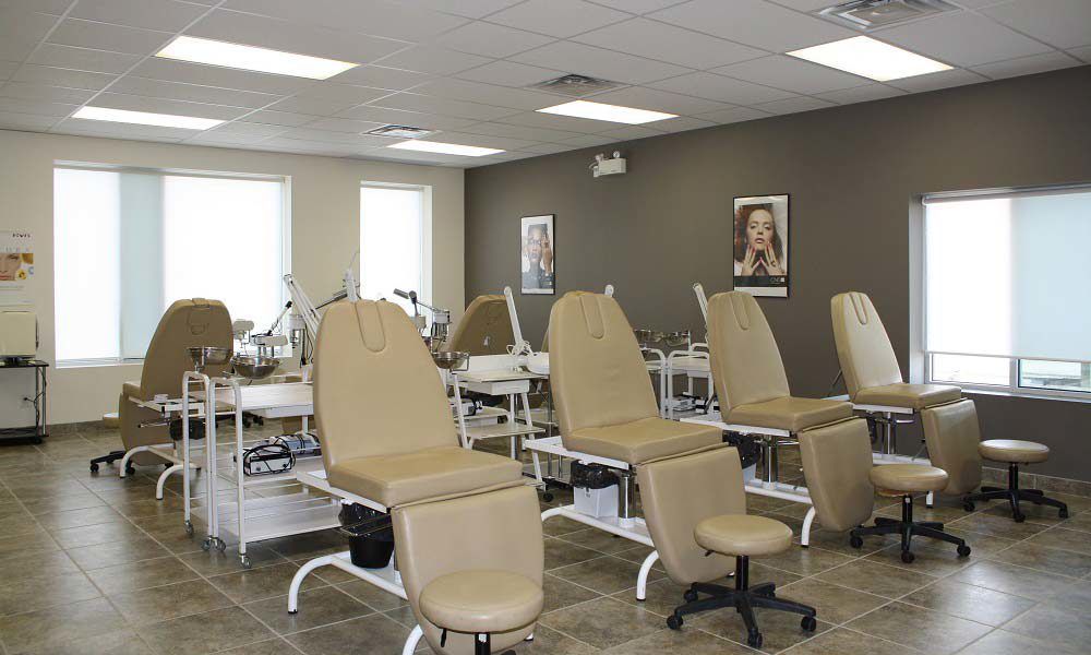 Salon interior with manicure stations and beige chairs, near windows and gray wall.