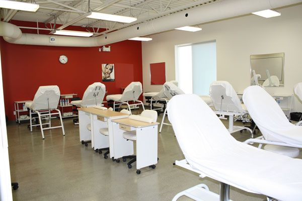 Nail salon interior with white chairs, manicure tables, red accent wall, and bright lighting.