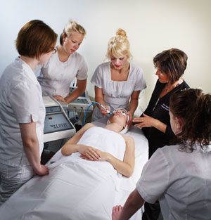 Esthetics students observe a facial treatment on a client in a spa setting.
