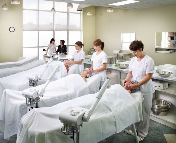 Salon students practicing facials on clients in a well-lit classroom.