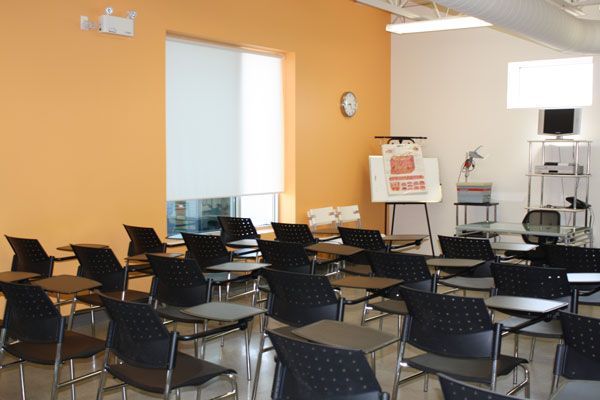Classroom with desks, chairs, whiteboard, and projector screen; orange and white walls.