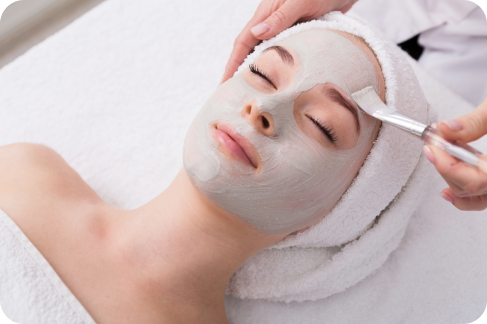 Woman receiving a facial mask in a spa; white towel, application with a brush.
