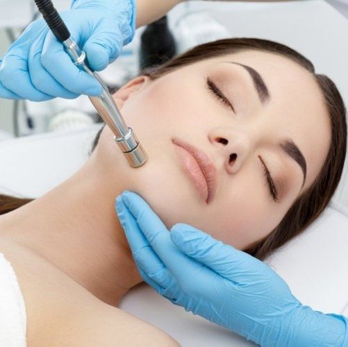 Woman receiving a facial treatment with a handheld device, blue gloves.