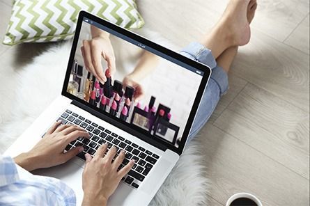 Person using laptop on floor, watching makeup tutorial, with coffee.
