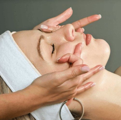 Woman receiving facial massage, eyes closed, hands on face.