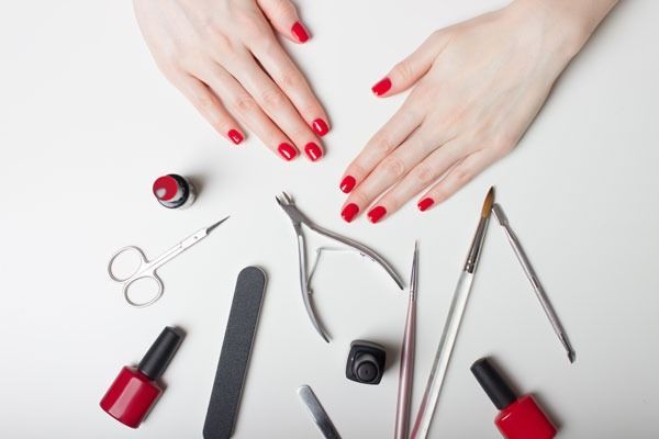 Hands with red nail polish surrounded by nail care tools on a white surface.